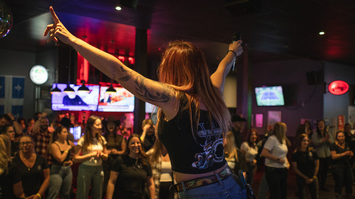 Soirée de danse en ligne dans un bar : bras dans les airs devant une salle pleine
