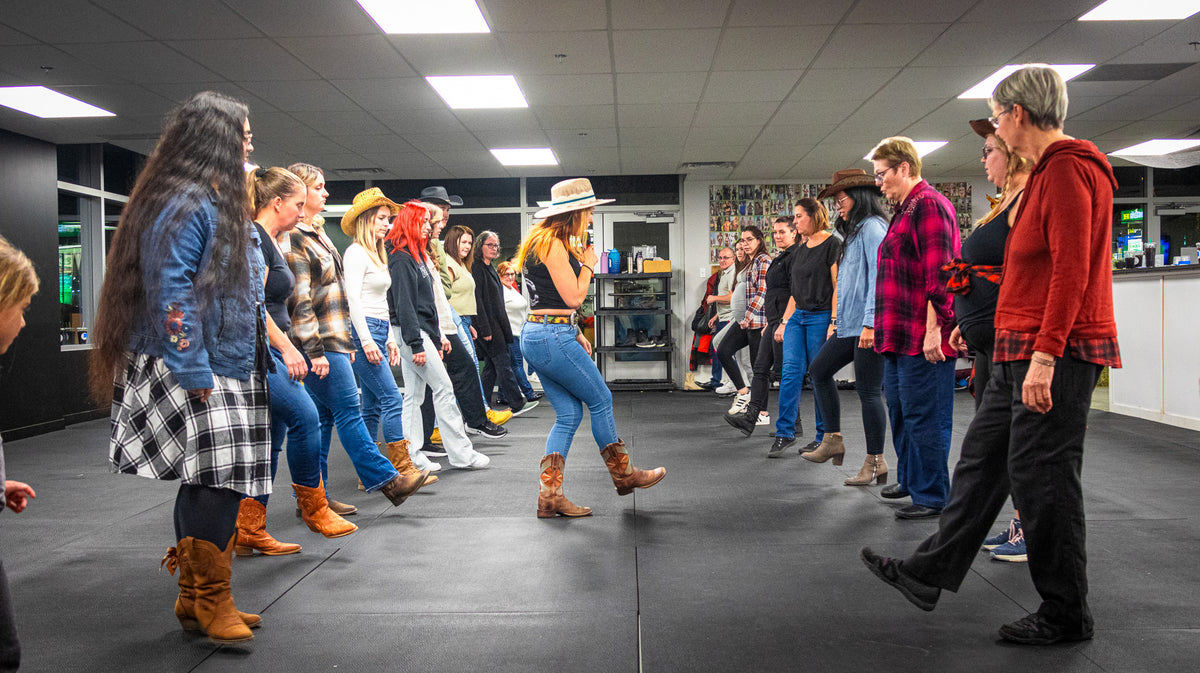 Une rangée de danseurs en bottes suit l'instructrice pendant un cours
