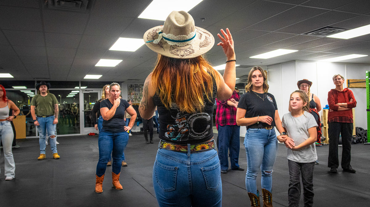 Une femme au chapeau lance la danse devant un groupe en studio, bras dans les airs