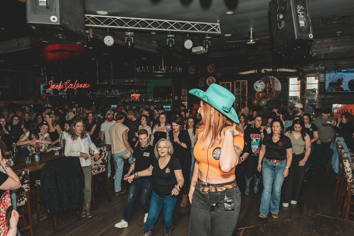 Au micro, une personne au chapeau turquoise guide une salle pleine qui danse en ligne