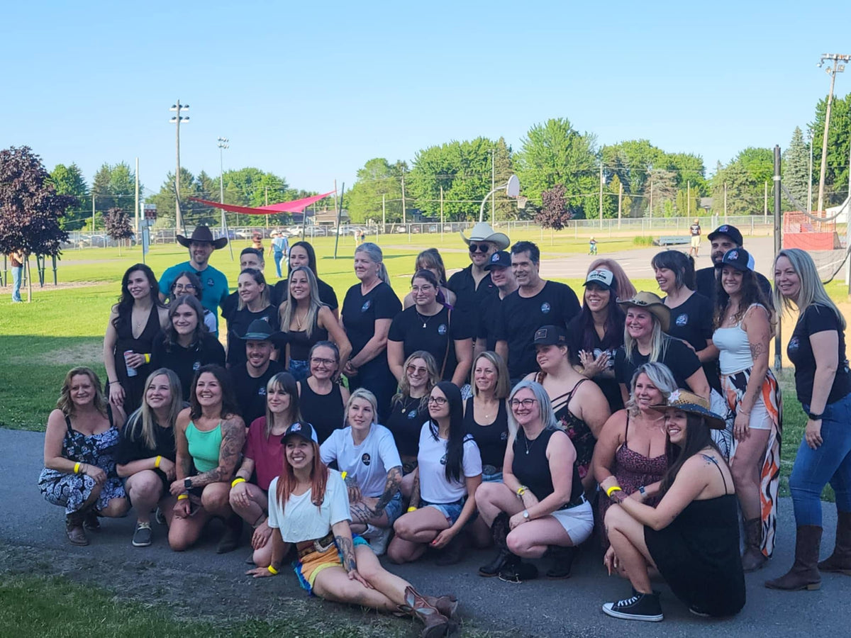 Un grand groupe tout sourire pose en rangées dans un parc ensoleillé, plusieurs en t-shirts noirs assortis